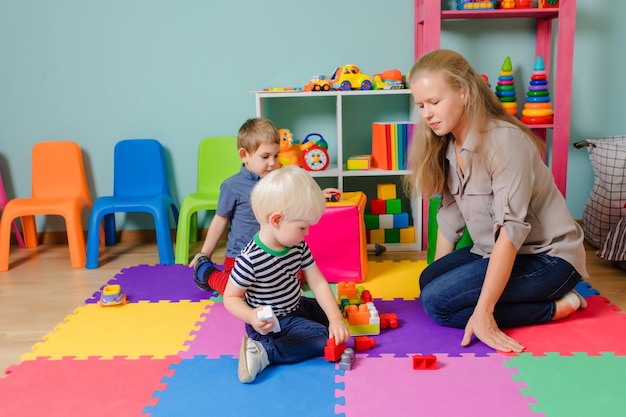 The teacher with kids are sitting on the floor and playing Boy play with construction blocks