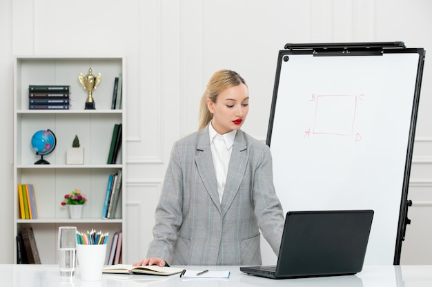 Teacher young cute instructor in suit in classrom with laptop and whiteboard typing on laptop