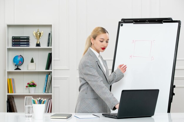 Teacher young cute instructor in suit in classrom with laptop and whiteboard typing on laptop