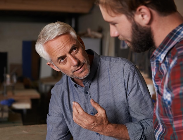 Photo teaching father and son in a workshop discussion and skills with development growth and bonding family parent and dad with grown up child planning and lesson with guidance startup and talking