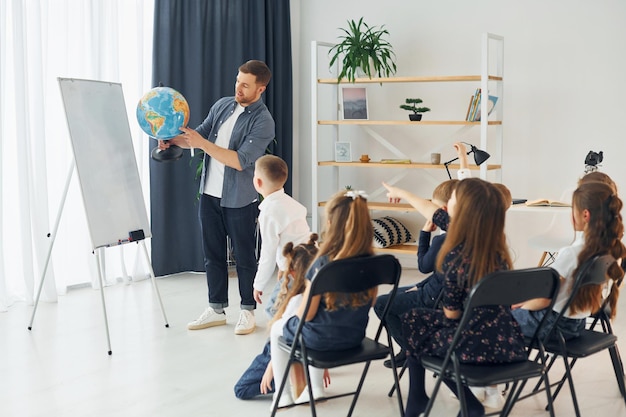 Teaching geography lesson by using earth globe group of\
children students in class at school with teacher