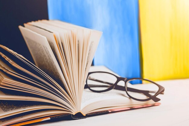 Teaching the Ukrainian language An open book and glasses lie on the table against the background of the Ukrainian flag