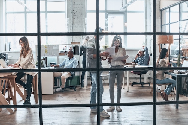 Foto team aan het werk. volledige lengte van jonge moderne mensen die samen werken en communiceren terwijl ze achter de glazen wand in de bestuurskamer staan