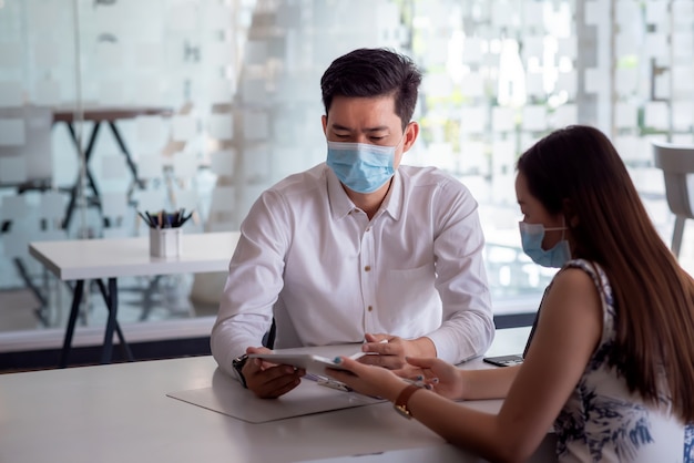 Team Asian Business people analyze collaboration using tablet in the office with wearing masks.