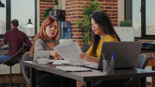 Team di donne asiatiche che fanno brainstorming di idee strategiche in ufficio, avviando una partnership per aiutare la crescita dell'azienda. colleghi che lavorano con statistiche finanziarie e scartoffie per lo sviluppo.