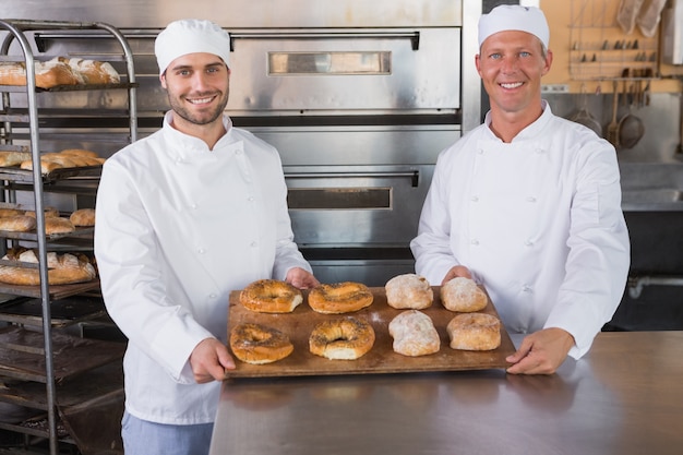 Team of bakers smiling at camera with trays of bread