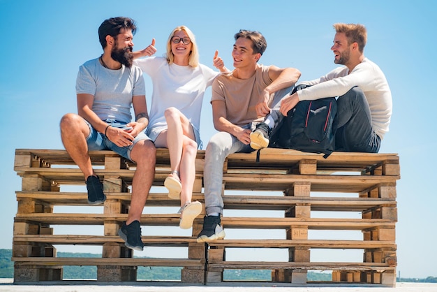 Team of best friends spend their carefree time communicating and sitting on bench at summer blue sky...