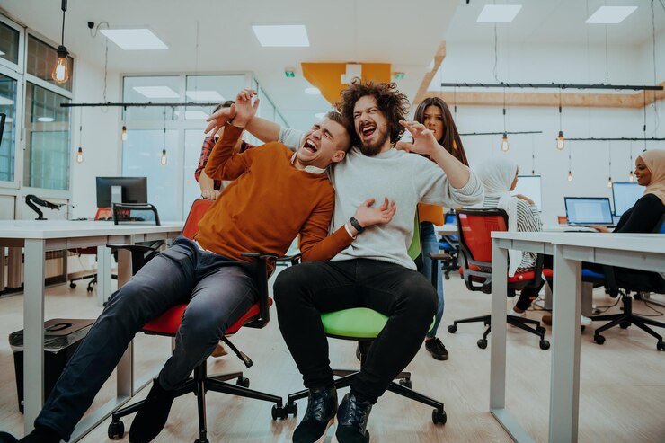 Photo team building and office fun young cheerful businesspeople in smart casual wear having fun while racing on office chairs and smiling