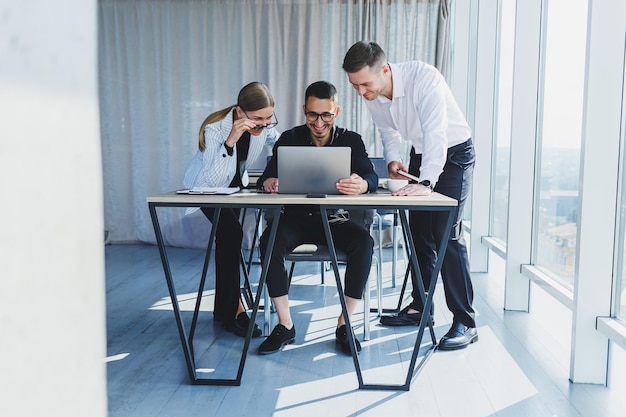 A team of businessmen in formal wear discussing project details\
and looking at laptop screen while collaborating during a meeting\
in a modern boardroom modern office