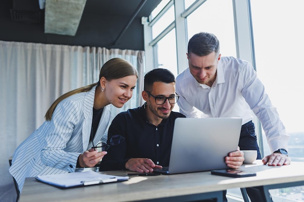 A team of businessmen in formal wear discussing project details and looking at laptop screen while collaborating during a meeting in a modern boardroom Modern office