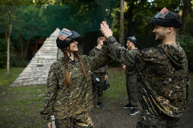 Team in camouflage and masks playing paintball, war on playground in the forest. Extreme sport with pneumatic weapon and paint bullets or markers, military game outdoors, combat tactics