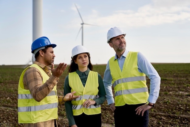 Team of caucasian and latin engineers standing on wind turbine field and discussing