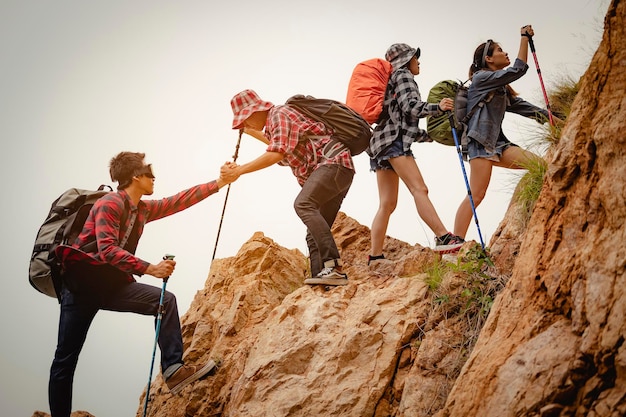 登山の成功のためのハイキングのための赤い旗で丘を上って互いに助け合うために手をつないでいる登山家の男性と女性のハイカーのチーム。ハイキング、ハイカー、チーム、山、登山、アクティビティのコンセプト。