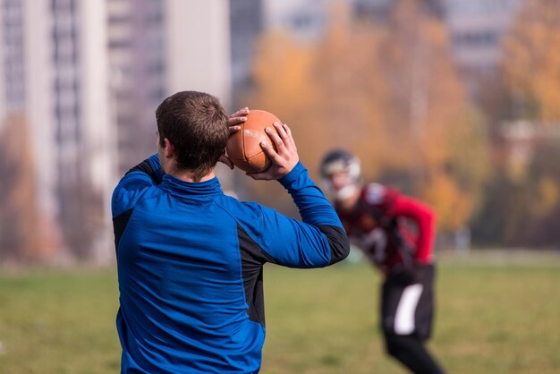 Photo team coach throwing the ball into the group of young american football players in action during the training at the field