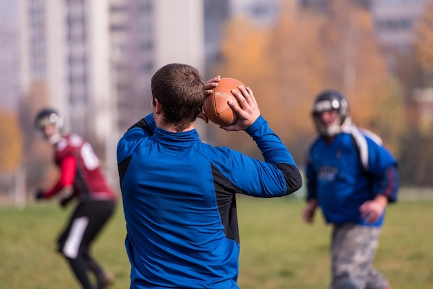 Team coach throwing the ball into the group of young american football players in action during the training at the field