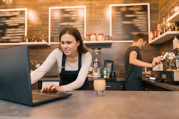 Photo team of coffee shop workers working near the counter with laptop computer and making coffee,