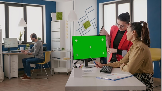 Team of colleagues using green screen on computer in business office. Coworkers looking at chroma key display with isolated background and mock up copy space template on monitor.