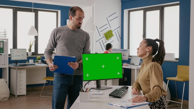 Team of coworkers using computer with green screen in startup office. Man and woman working with isolated chroma key template and mock up background, having conversation at job.