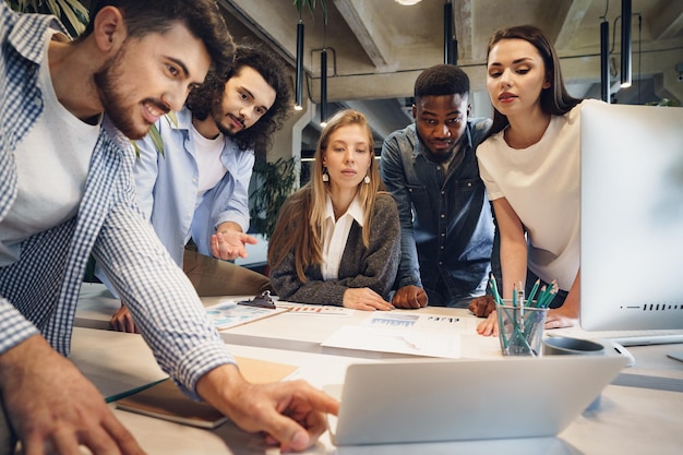 Team of diverse coworkers in modern office discuss their project together