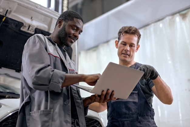 team of diverse mechanics in uniform examining car using laptop while working in auto service black