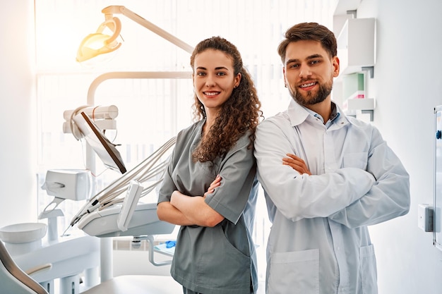 Photo a team of doctors in a dental office standing back to back and looking at the camera and smiling the work and leisure of doctors in the background a dental chair and equipment copy spacesunlight