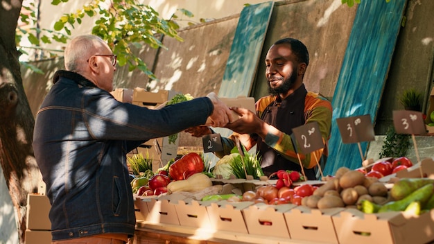 Team of farmers selling natural homegrown products to group of customers, talking to people about health benefits. Local vendors business owners giving box of fresh seasonal produce. Handheld shot.