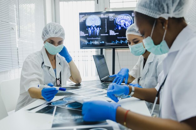 Команда женщин-врачей проверяет результаты сканирования на бумаге и смотрит на мониторы в лаборатории, делится медицинскими знаниями и опытом, пользуется своими коллегами и пациентами перед операцией и лечением.