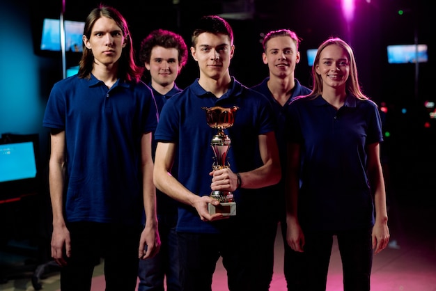 Team of five young champions in cybersports and network gaming competition standing in row in contemporary e-sports club