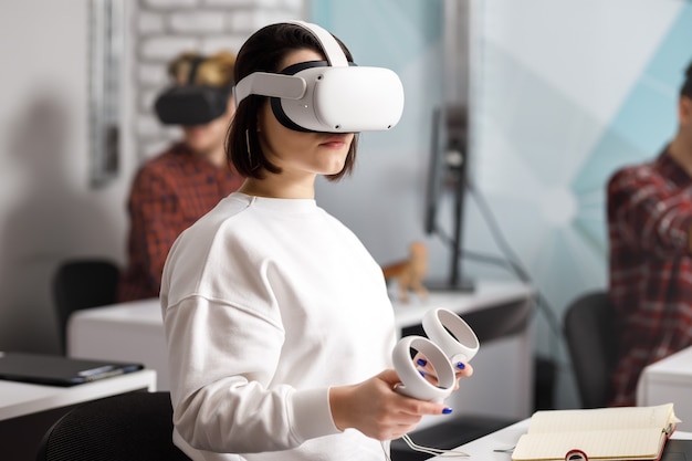 Team of four creative engineers working with virtual reality, young woman testing VR glasses or goggles sitting in the office room