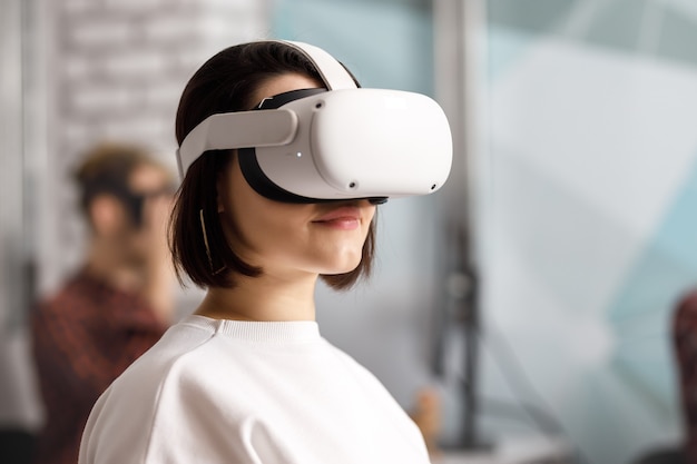Команда из четырех креативных инженеров, работающих с виртуальной реальностью, молодая женщина тестирует очки виртуальной реальности или очки, сидя в офисном помещении