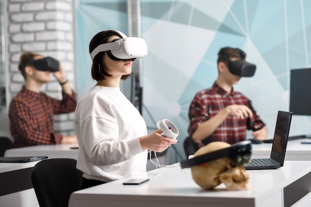 Team of four creative engineers working with virtual reality, young woman testing VR glasses or goggles sitting in the office room