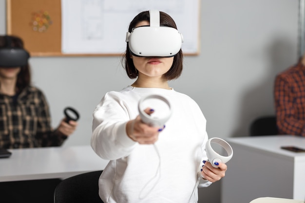 가상 현실 작업을하는 4 명의 창의적인 엔지니어 팀, 사무실 방에 앉아 VR 안경 또는 고글을 테스트하는 젊은 여성