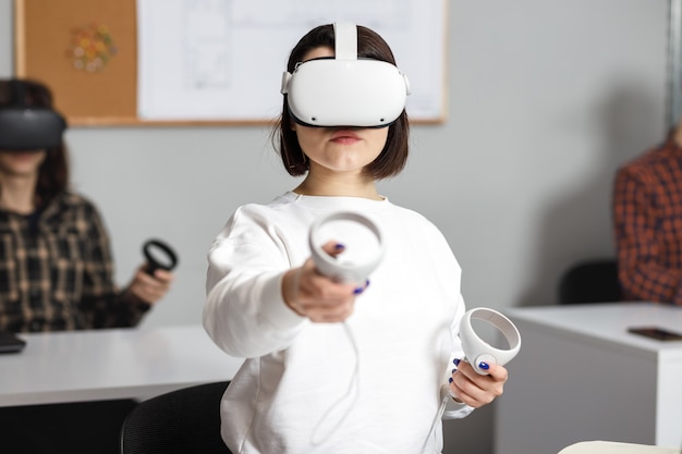 Team of four creative engineers working with virtual reality, young woman testing VR glasses or goggles sitting in the office room