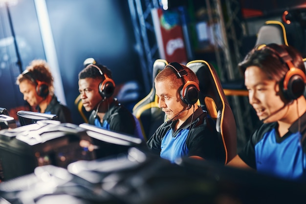 Team of four professional cybersport gamers wearing headphones participating in esport tournament