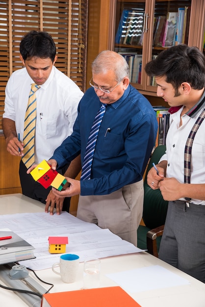 Team of Indian architects or builders drafting or discussing housing project with the building model and plan around conference table selective focus