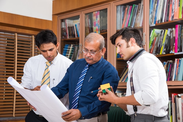 Team of Indian architects or builders drafting or discussing housing project with the building model and plan around conference table selective focus