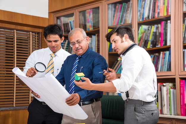 Team of Indian architects or builders drafting or discussing housing project with the building model and plan around conference table selective focus