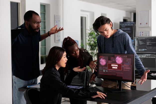 Team of it programmers having web server hacked, looking at critical error on computer monitor in big data office. Diverse software developers trying to solve hacking problem, firewall security.