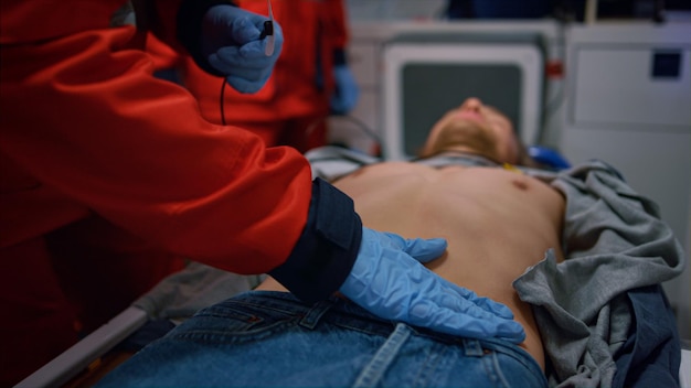 写真 救急車で患者を救助する救急医師のチーム 救急医の手は男性にホルターモニターデバイスを適用し 医療従事者は手袋をかぶって 被害者の心臓の電気活動をチェックしています