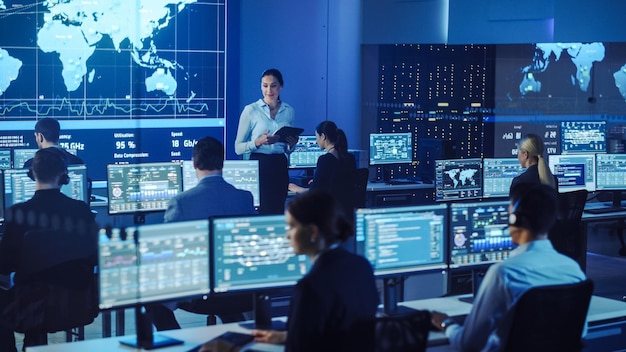 team of professional computer data science engineers work on desktops with screens showing charts graphs infographics technical neural data and statistics dark control and monitoring room