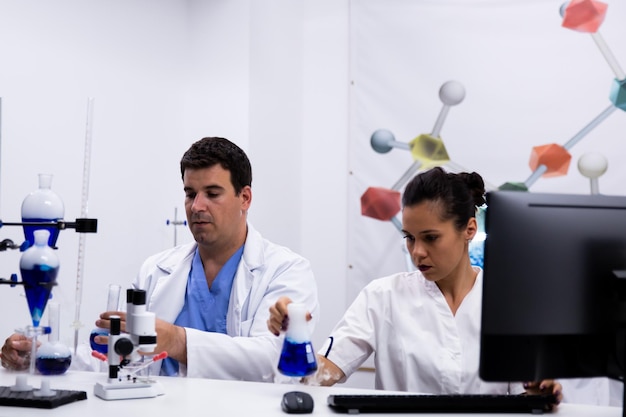 Team of researchers wearing their coat in research laboratory. Female researcher looking at test tube with blue liquid.