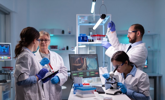 Team of scientific investigators conducting experiments in lab using microscope and micropipette