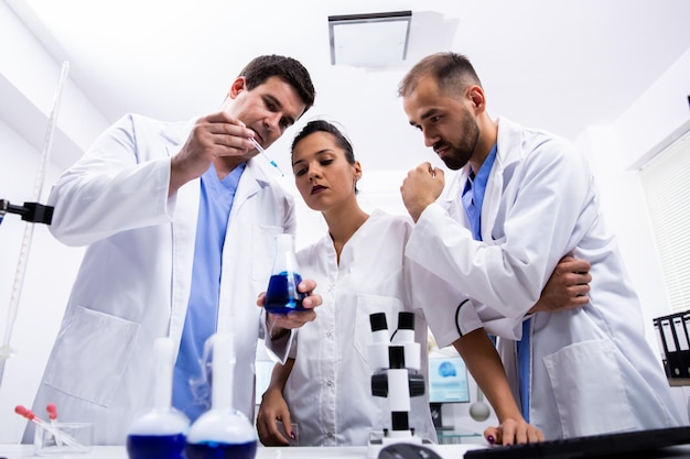 Foto squadra di scienziati in camice bianco che esaminano un campione di liquido blu fumante nel laboratorio di ricerca.