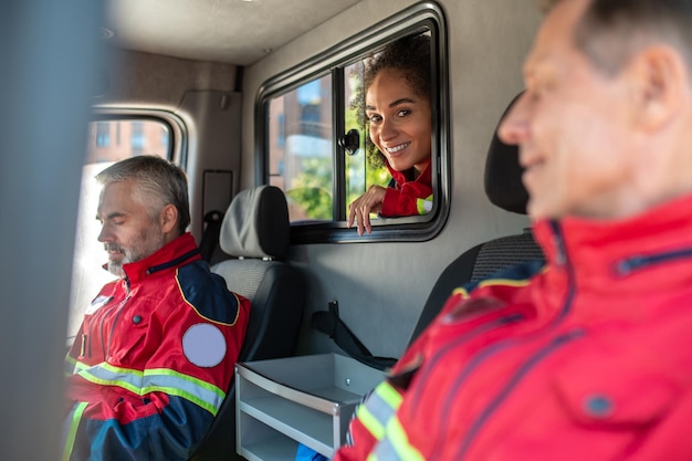 Foto squadra di paramedici sorridenti e contenti in uniformi rosse seduti insieme nel veicolo di emergenza medica