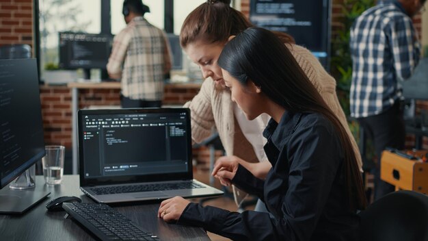 Team of software developers talking about source code running on laptop screen while sitting at desk artificial intelligence server room. Database admins collaborating on data coding group project.