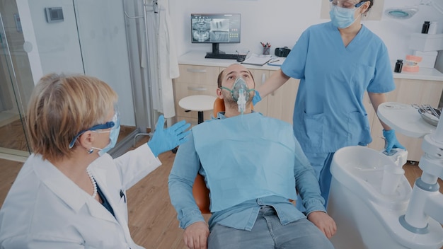 Team of specialists doing anesthesia on patient in dentistry\
office. nurse applying oxygen mask on face, giving anesthesic to\
man before beginning stomatological procedure in cabinet.