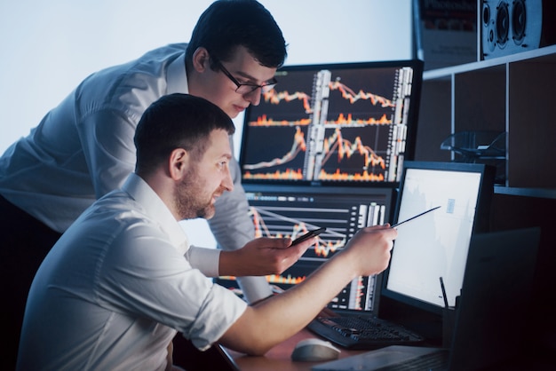 Team of stockbrokers are having a conversation in a dark office with display screens. analyzing data, graphs and reports for investment purposes. creative teamwork traders