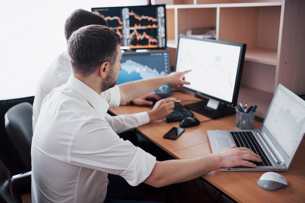 Team of stockbrokers are having a conversation in a dark office with display screens. Analyzing data, graphs and reports for investment purposes. Creative teamwork traders