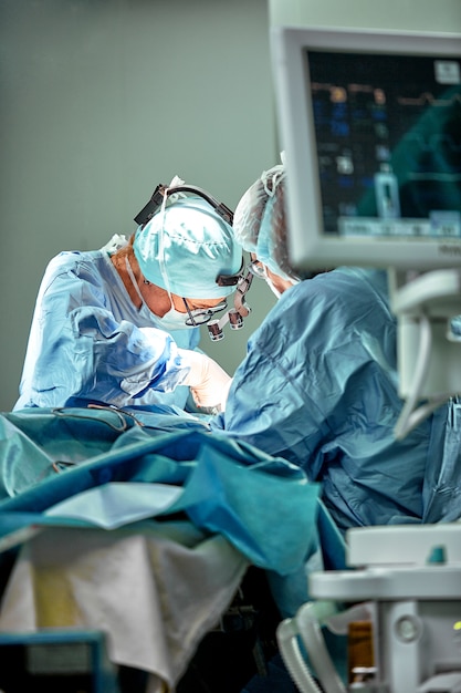 수술실에서 일하는 외과 의사 팀. 몇몇 외과의 사는 실제 수술실에서 수술을하고 있습니다. 푸른 빛, 흰 장갑 세로 샷입니다.