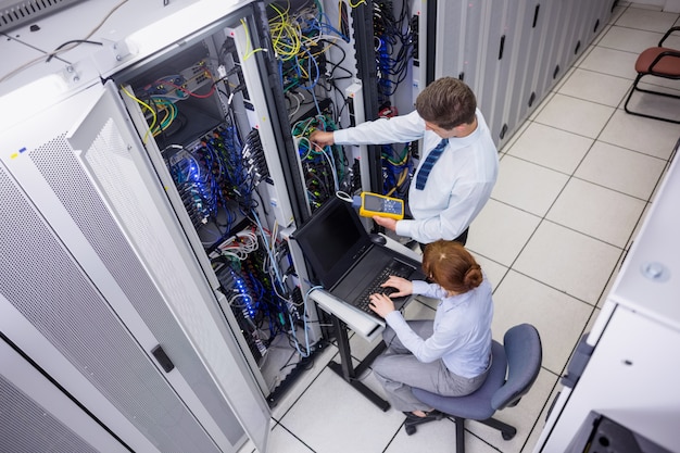 Team of technicians using digital cable analyser on servers